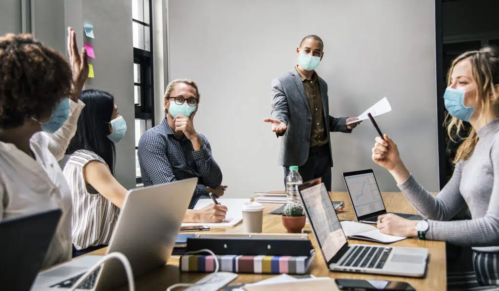 O que as empresas estão fazendo para ajudar seus colaboradores no ambiente pós-pandemia? 2 business people wearing masks in coronavirus meeting the new normal